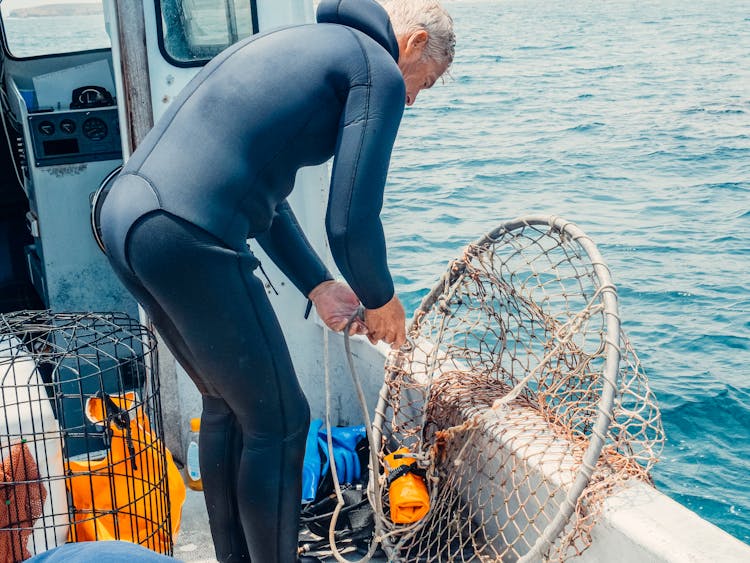 A Scuba Diver Fixing A Mesh Net Aboard A Boat