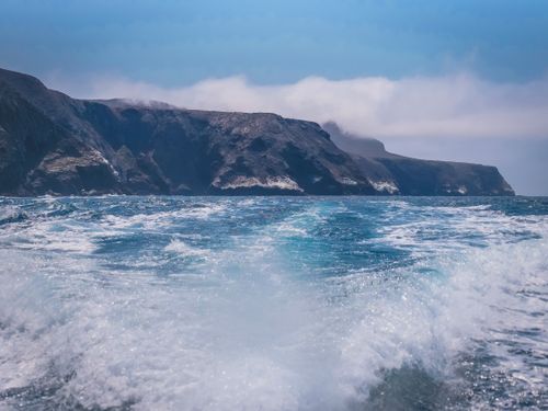 Free Vibrant ocean waves crash against stunning coastal cliffs under a clear blue sky. Stock Photo