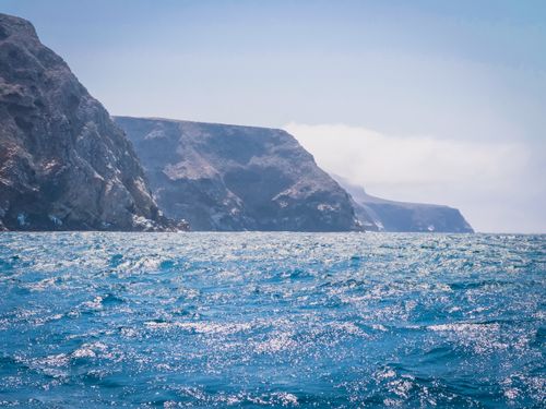 Free A stunning view of rugged cliffs by a shimmering blue ocean on a clear day. Stock Photo