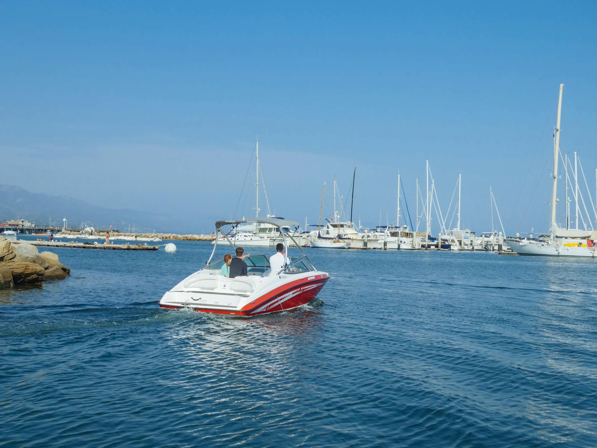 A motorboat navigates through a tranquil marina with yachts and clear blue skies in the background.