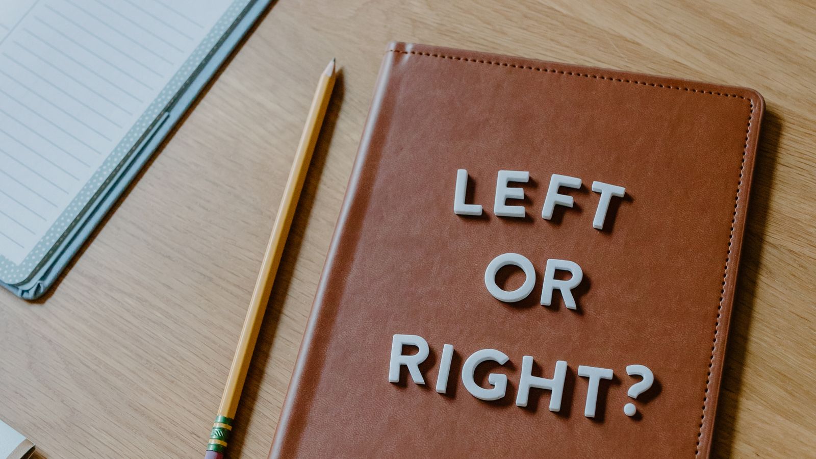 An open notebook with “Left or Right?” beside a laptop and pencil on a desk