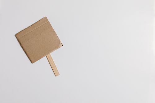 Free A simple cardboard sign on a stick placed against a clean white background in a minimalist style. Stock Photo