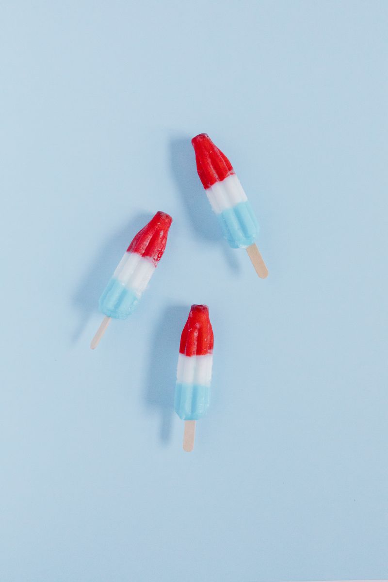 Three vibrant red, white and blue layered ice pops on a light blue background