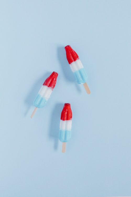 Free Three vibrant red, white, and blue ice pops on a light blue background, perfect for summer or Fourth of July themes. Stock Photo