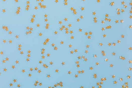 Gold star confetti scattered over a light blue surface, perfect for festive occasions.