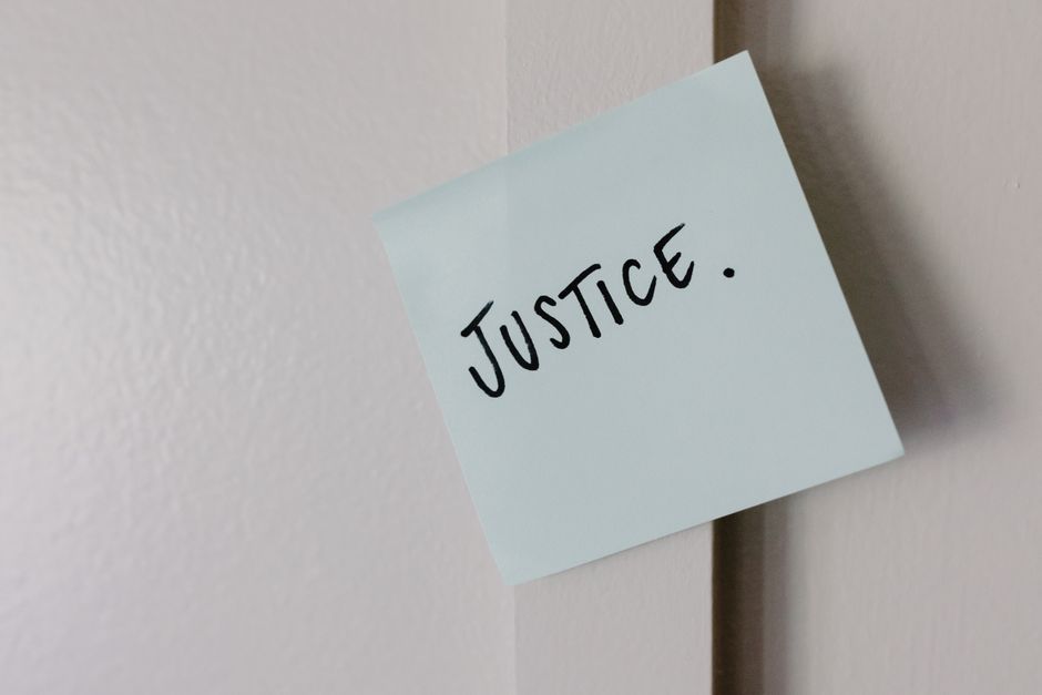 A sticky note with handwritten 'Justice' message on a white wall.