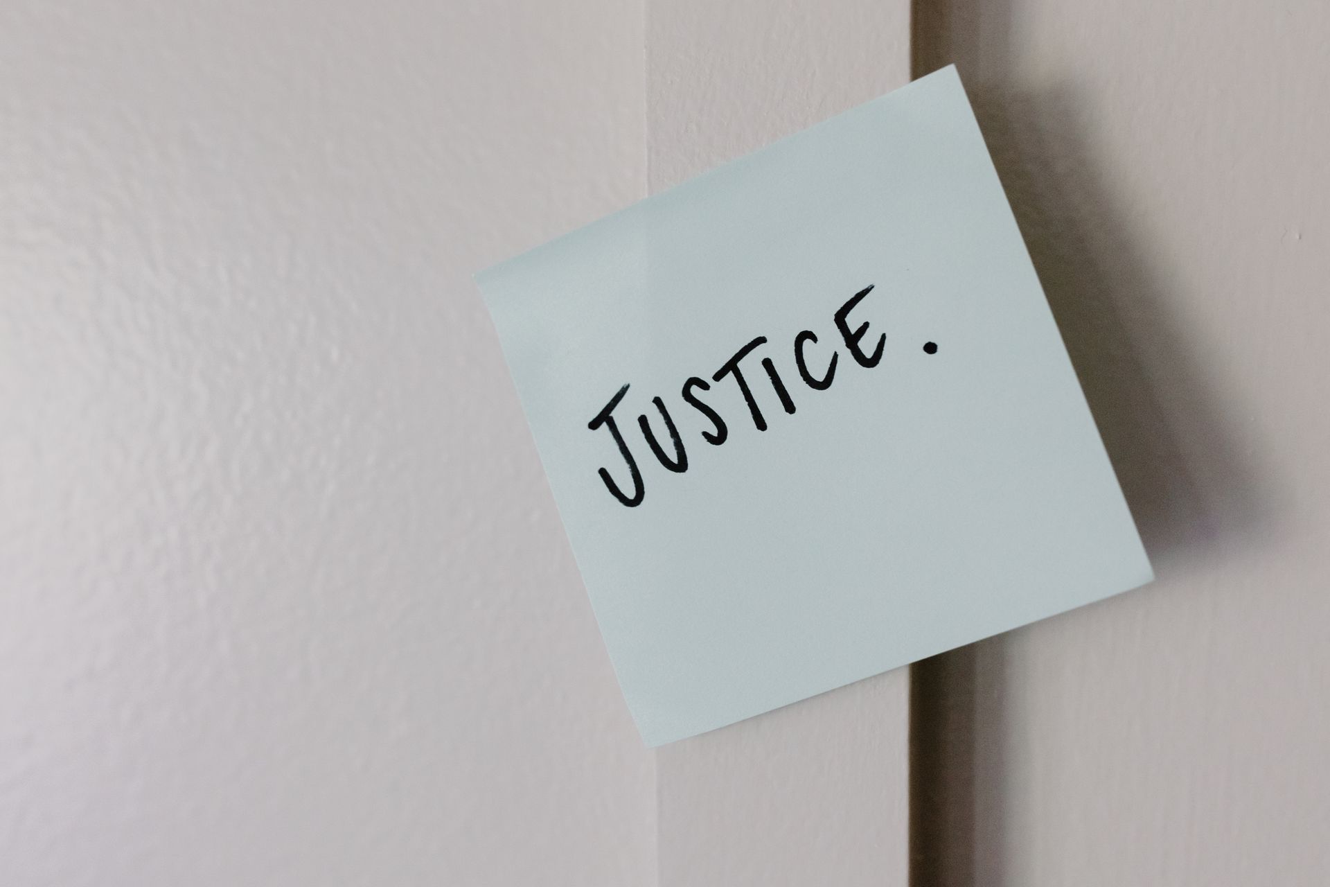 A sticky note with handwritten 'Justice' message on a white wall.