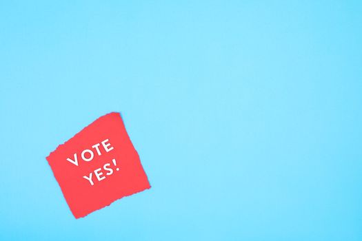 Red paper with 'Vote Yes!' text on a bright blue background promoting positive political engagement.