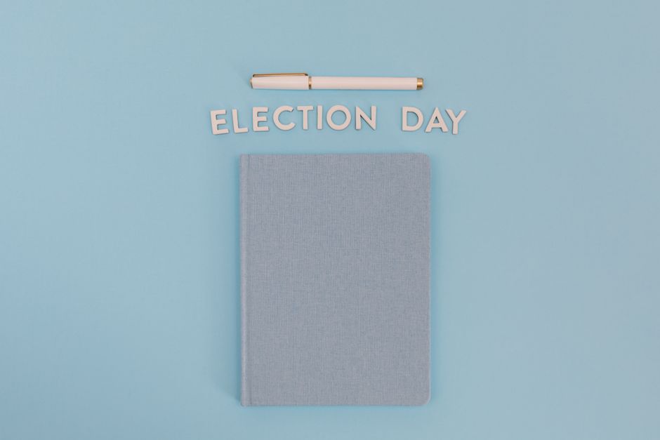 Vista plana de un cuaderno y un bolígrafo con el texto 'Día de las Elecciones' sobre un fondo azul.