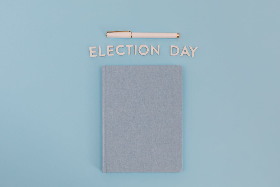 A Notebook, Pen and a Text Saying "Election Day" Lying on Blue Background 