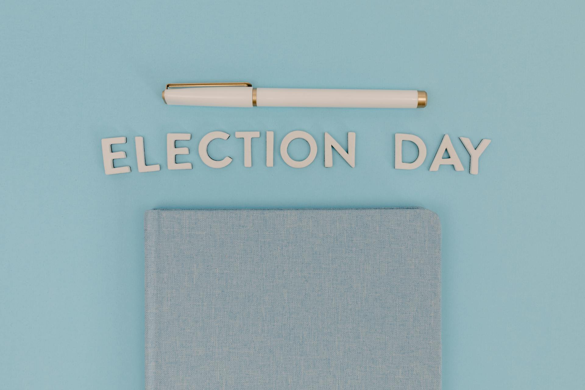 Blue notebook and pen against a light blue background reading 'Election Day', ideal for campaign themes.