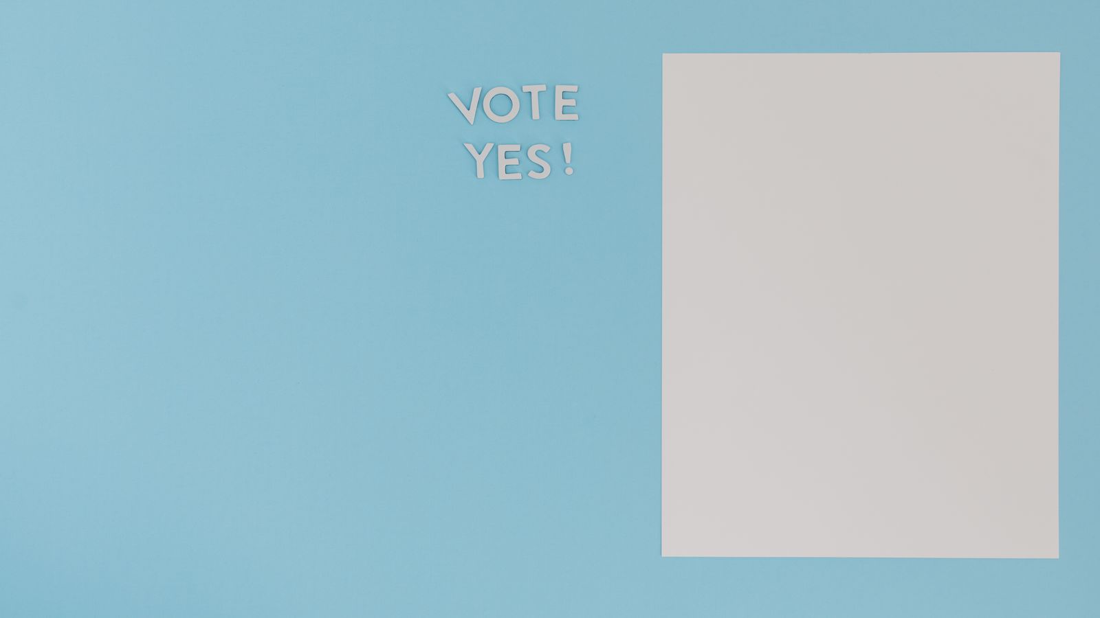 A minimalist concept image featuring 'Vote Yes' text and blank paper on a blue background.