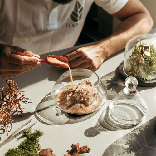 Free Close-up of a person creating a terrarium with sand, moss, and glass containers. Stock Photo