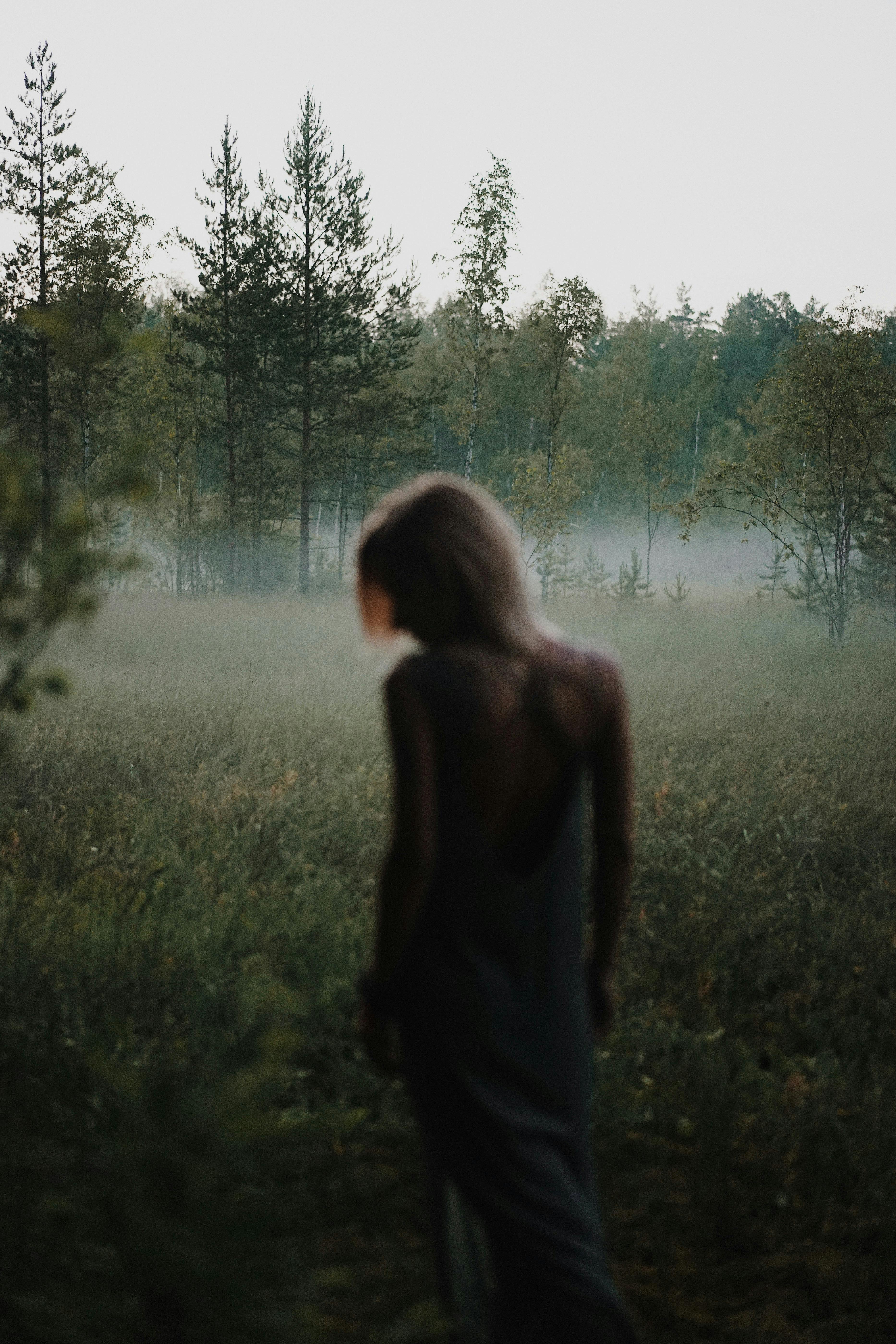 Moody shot of a woman standing in a foggy forest meadow, creating a mysterious atmosphere.