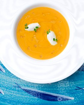A delicious gourmet pumpkin soup garnished with cream and herbs, served in an elegant white bowl.