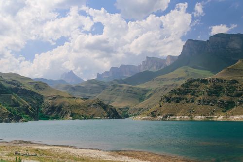 Free Breathtaking view of a serene lake surrounded by mountains under a cloudy blue sky. Stock Photo