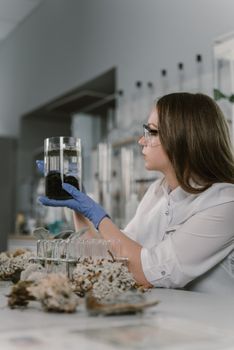 A female scientist wearing safety gear examines a sample in a laboratory setting.