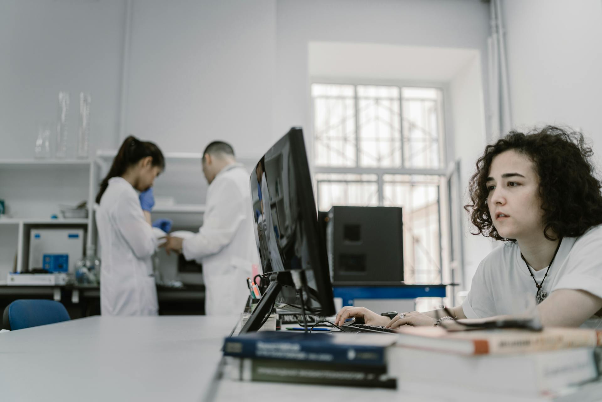 Focused woman working on a computer in a busy laboratory setting, showcasing teamwork and scientific research.