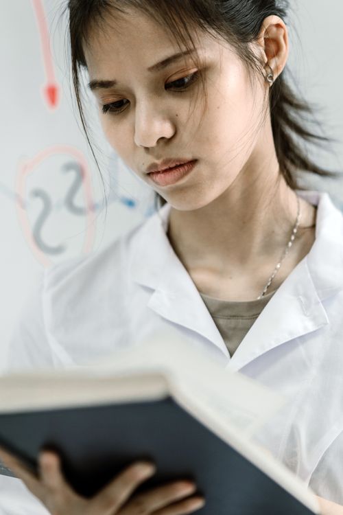 Free Asian female scientist in lab coat reading a book, experimenting in a laboratory setting. Stock Photo