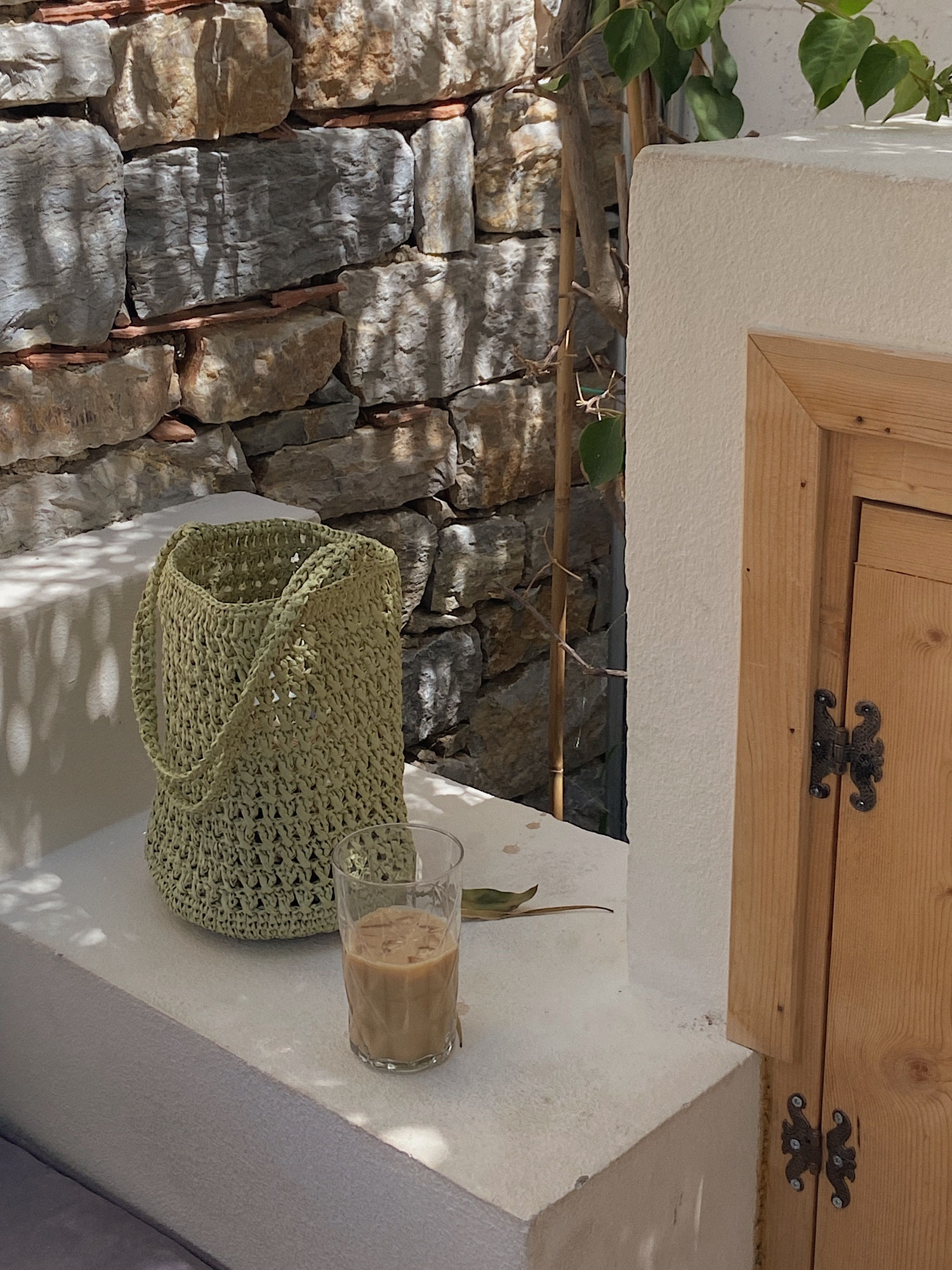 Cozy outdoor scene featuring a glass of iced coffee and a woven tote bag against a rustic wall.