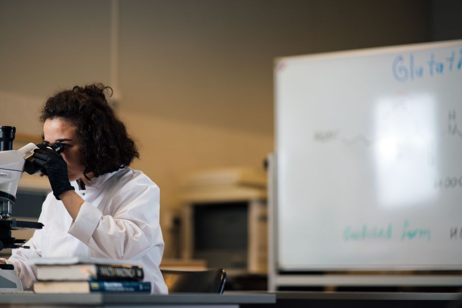 Female scientist examining samples under a microscope in a laboratory setting.