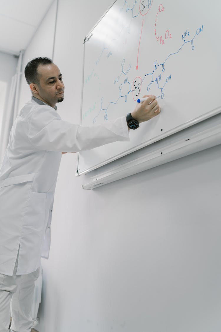 Man Wearing Lab Coat Writing Formula On White Board