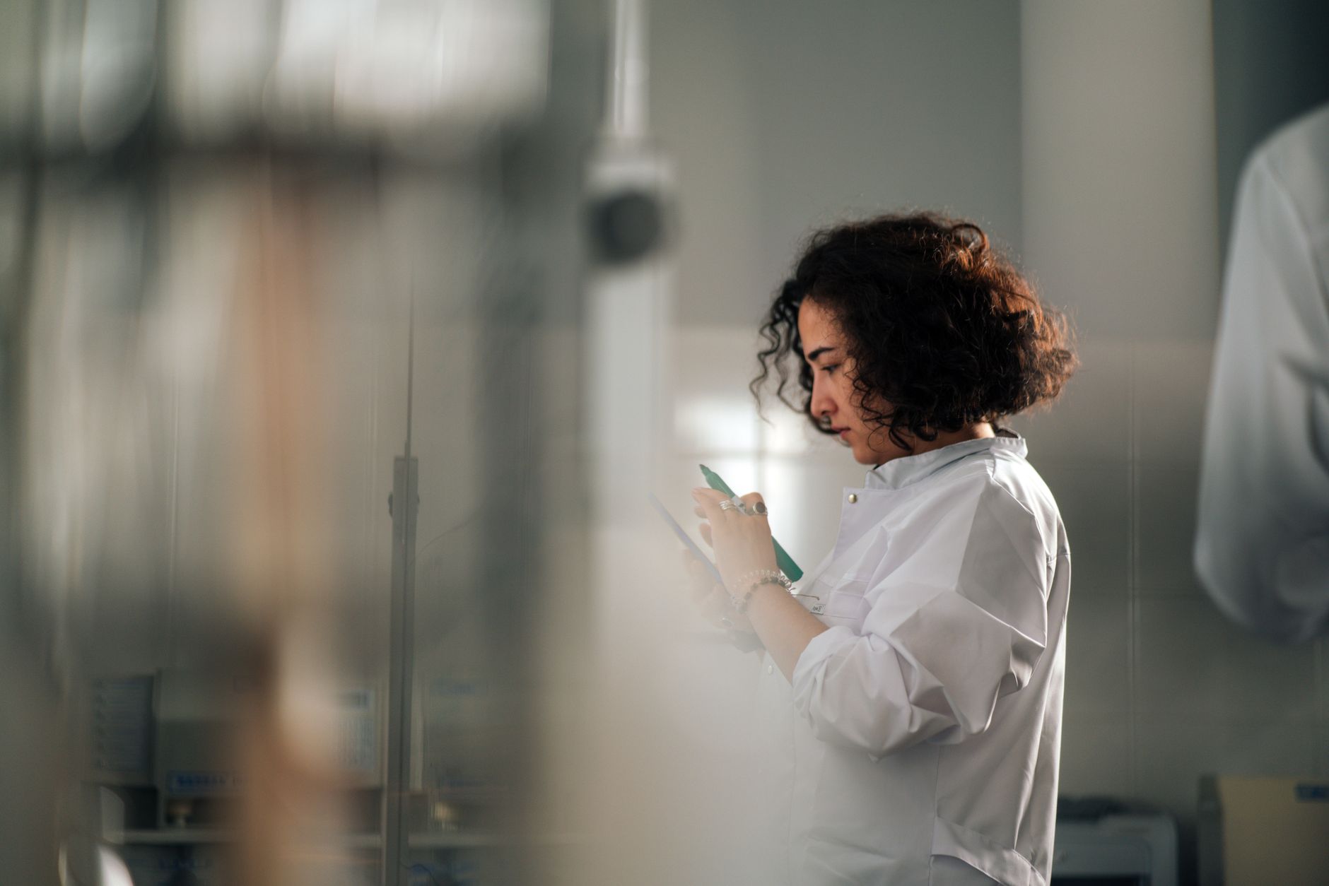 A focused female scientist with curly hair writes notes in a laboratory setting.