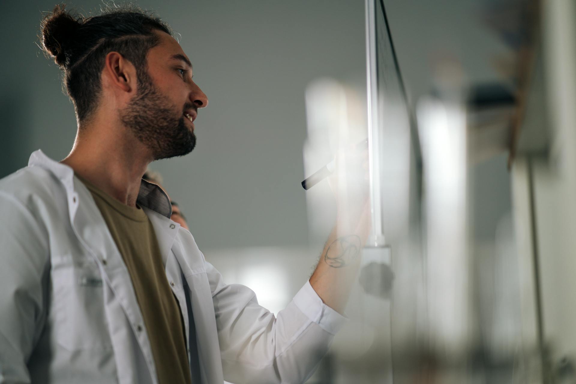 Young Man Wearing Lab Coat Writing Formula on White Board