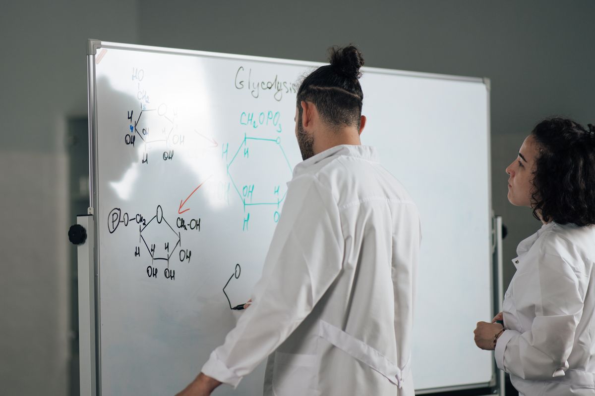 Two scientists discussing formulas written on a laboratory whiteboard