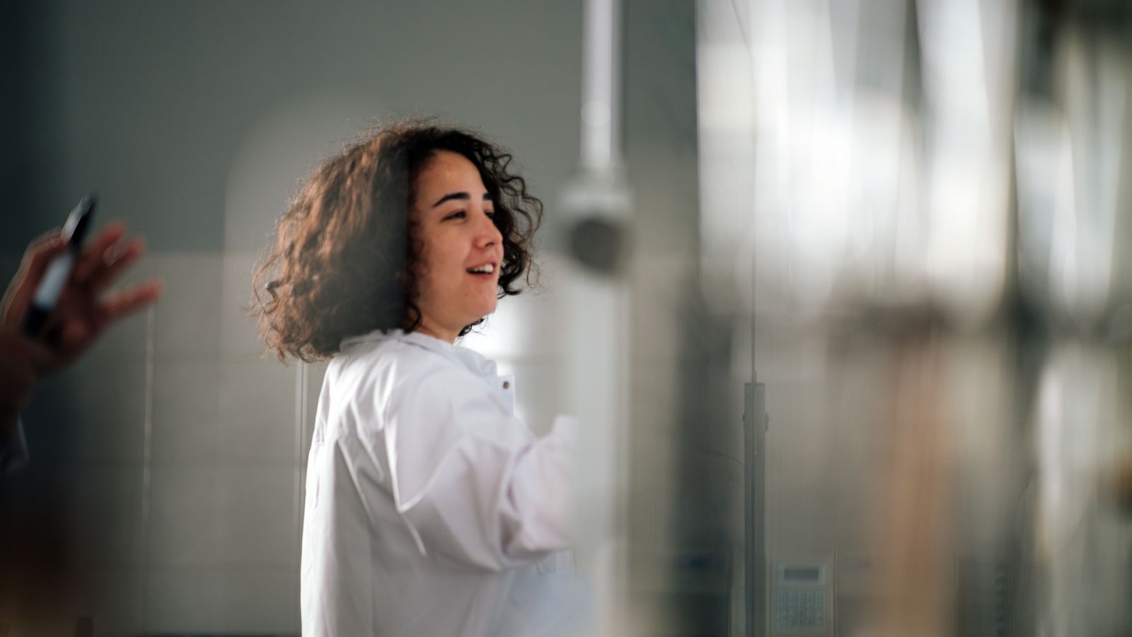 A young female scientist with curly hair in a lab coat working in a laboratory setting.