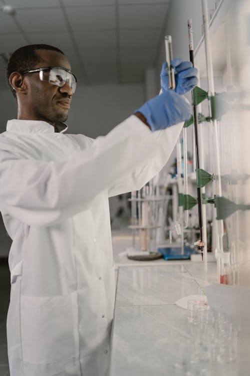 Man in White Lab Gown Wearing Protective Googles while Holding a Test Tube
