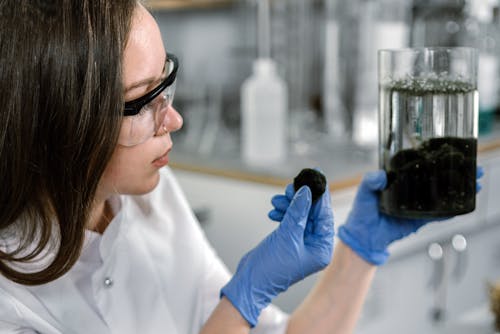 Woman in White Laboratory Coat Holding a Cylinder Glass