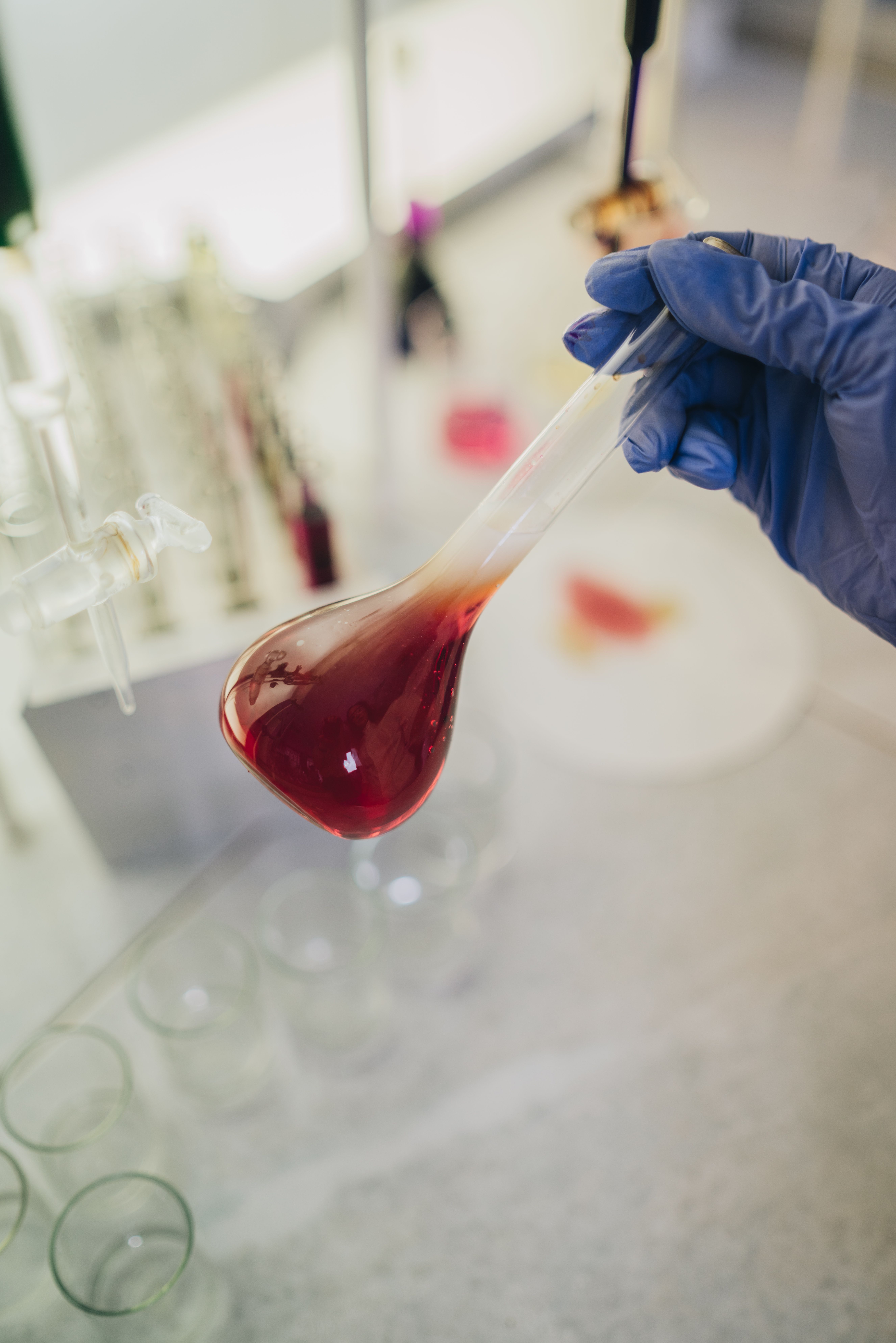 Close-up of a gloved hand holding a test tube with red liquid in a laboratory setting.