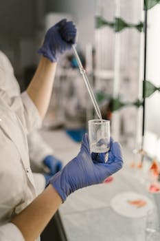 Scientist in a lab coat uses a dropper for chemical research in a laboratory setting.