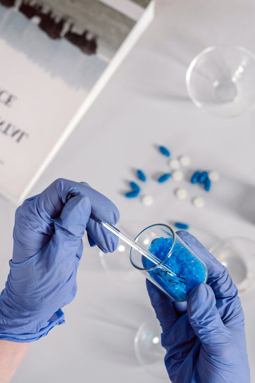 A Person Wearing Blue Latex Gloves Holding a Beaker