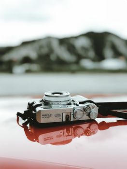 A vintage-style camera reflecting on a surface with a blurred mountain backdrop.