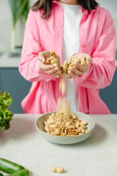 Person in pink shirt pouring mixed nuts into a bowl on a kitchen counter.
