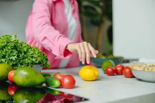 Free A person in a pink shirt reaching for a lemon surrounded by fresh vegetables. Stock Photo