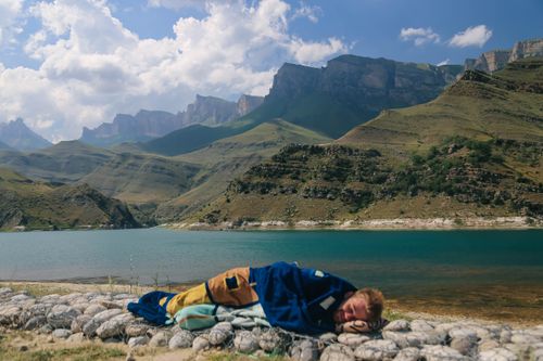 Free Man sleeping by a scenic lake and mountains in Russia, showcasing tranquil natural beauty. Stock Photo