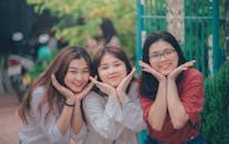 三位快乐的亚洲朋友在户外双手托腮，热情地微笑摆姿势