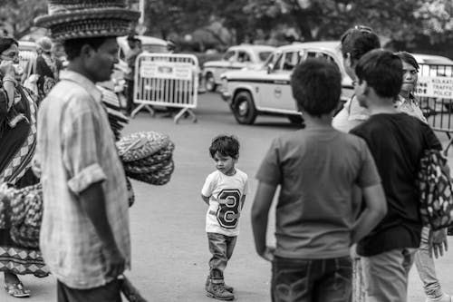 Black and White Photo of Little Boy Walking Alone on Street