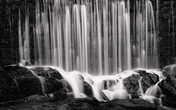 Black and white photo of a tranquil waterfall cascading over rocks.