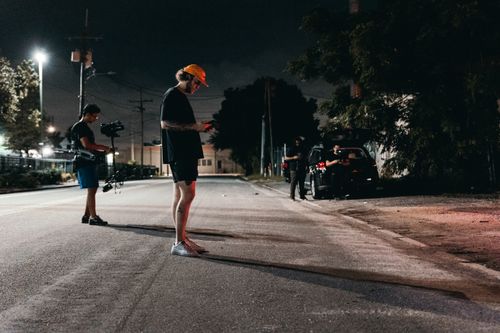 Free A camera crew sets up under streetlights for an outdoor nighttime film shoot on a quiet city street. Stock Photo