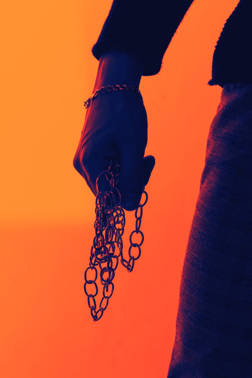 Artistic close-up of a hand holding a chain with an orange and blue color palette.