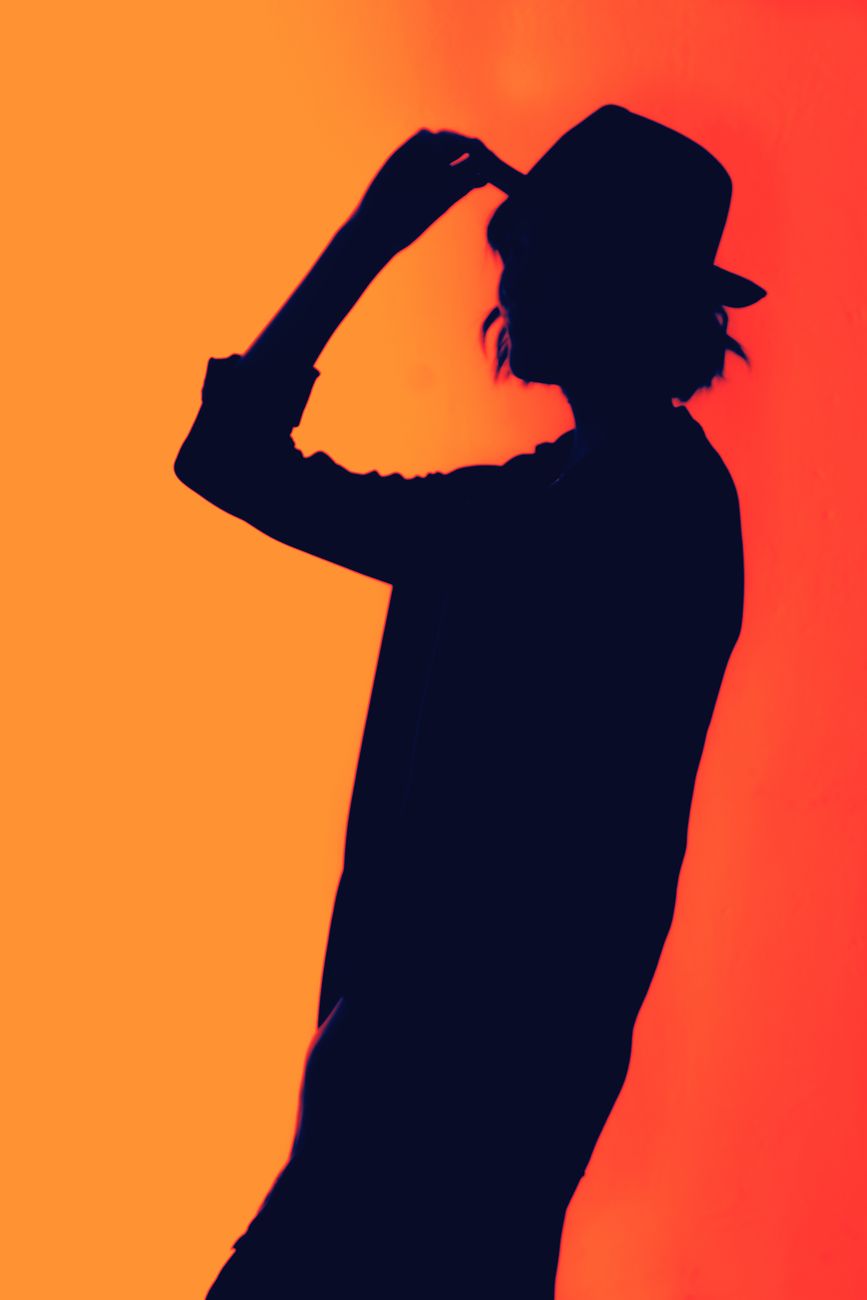 Silhouette of a person wearing a hat against a vibrant orange background, creating a striking contrast.