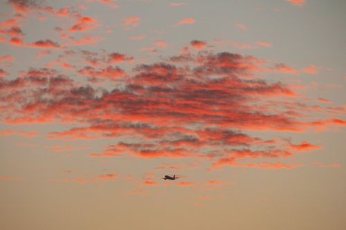 Free A silhouette of an airplane flying against a colorful sunset sky with dramatic clouds. Stock Photo