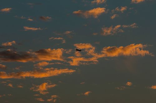 Free An airplane silhouette against a vibrant sunset sky, surrounded by clouds. Stock Photo
