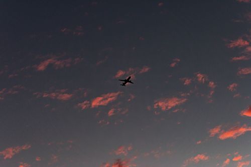 Free Silhouette of an airplane flying at sunset with vibrant clouds in the sky. Stock Photo