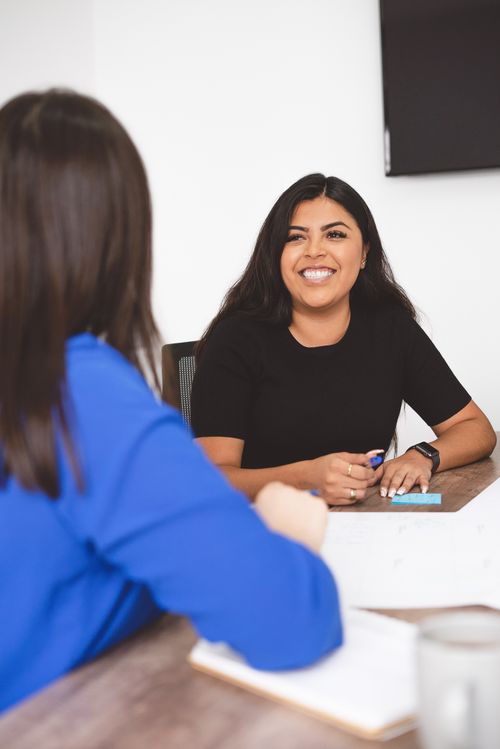Free Two women engaging in a business meeting, smiling confidently at each other in an office setting. Stock Photo
