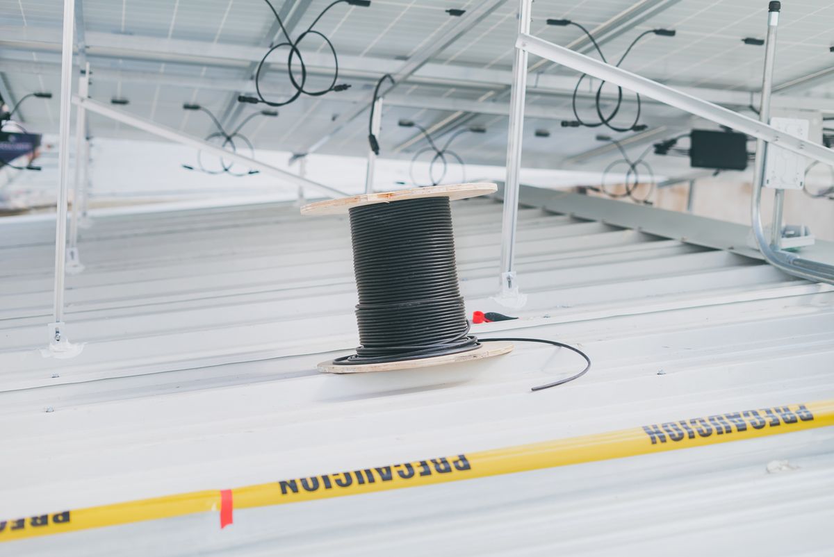 A coiled power cable on a commercial rooftop beside a solar array, with caution tape in the foreground